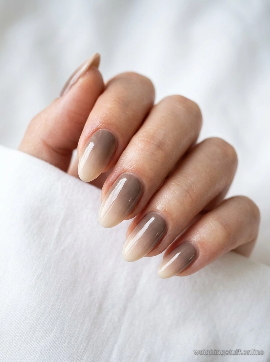 Close-up of taupe to cream subtle ombre nail design with high-shine topcoat against a white background.