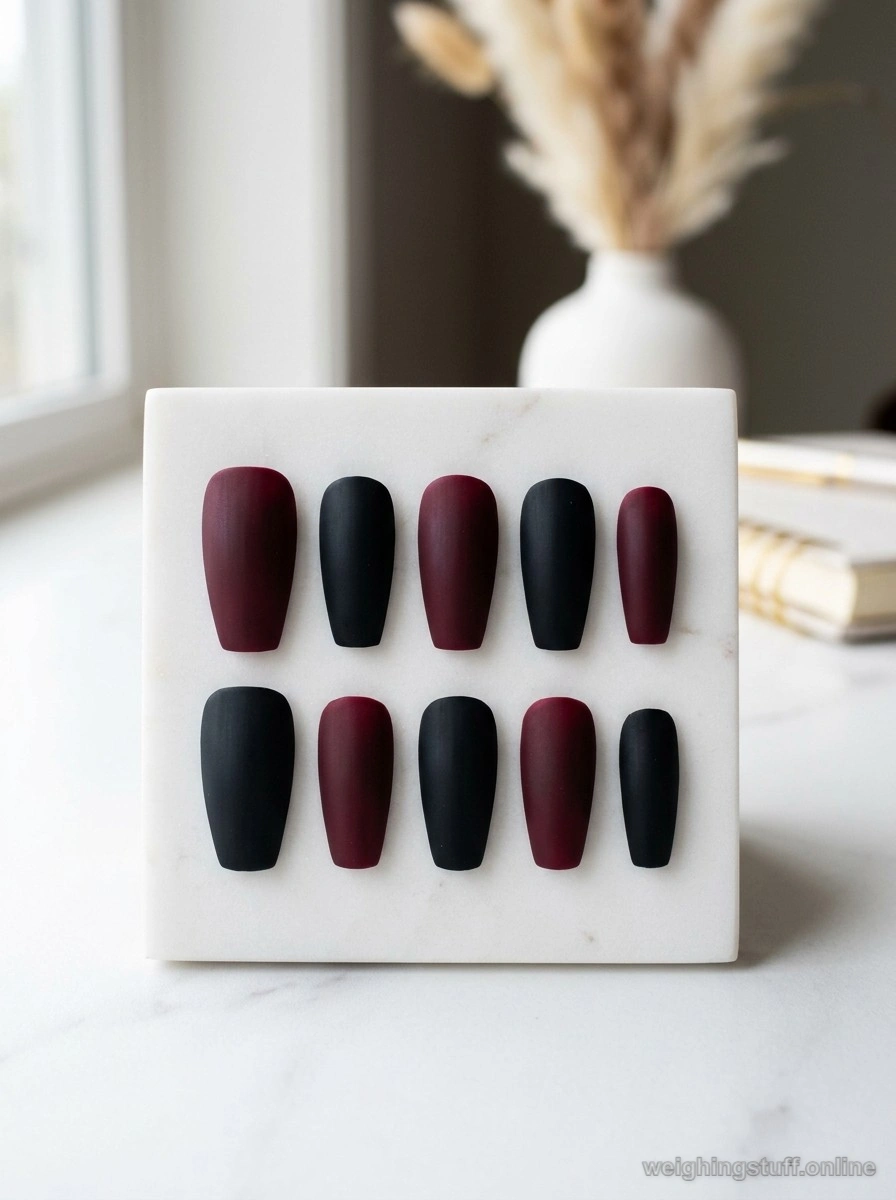 A sophisticated display of matte finish nails in deep burgundy and black on a minimalist white surface, emphasizing their velvety texture.