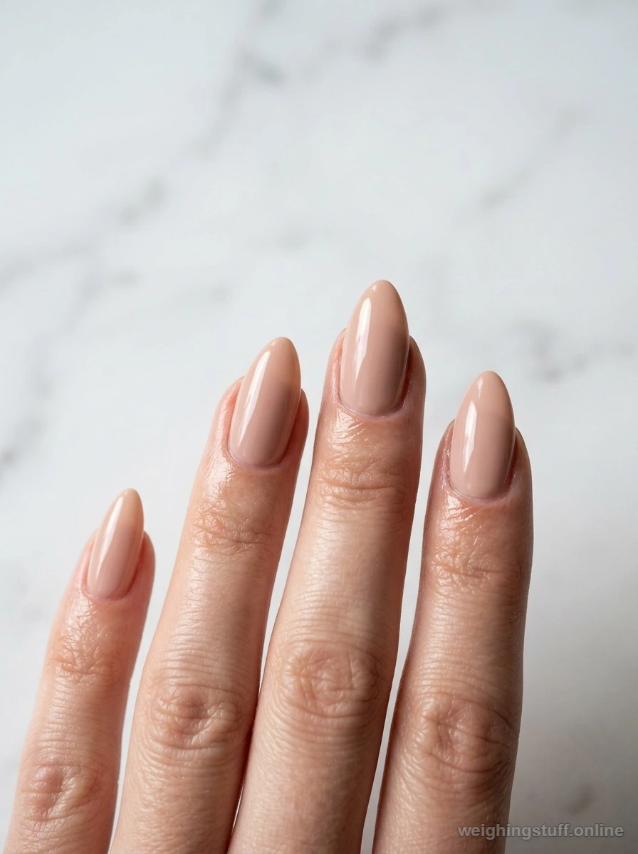 Close-up of neatly manicured nude almond-shaped nails against minimalist white marble, showcasing clean nail aesthetics.